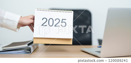Business woman change 2025 Year Calendar on table with laptop computer during working and writing in office. countdown, Happy New Year, Resolution, Year End and New Start and Goals Plan Action Concept 120089241