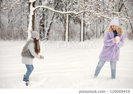 Young blonde woman with her daughter playing in winter in a snowballs. Caucasian woman wearing purple warm jacket and knitted hat. Brunette girl wearing grey jacket and hat. Young blonde woman with her daughter playing in winter in a snowballs. Caucasian woman wearing purple warm jacket and knitted hat. Brunette girl wearing grey jacket and hat. 120089459