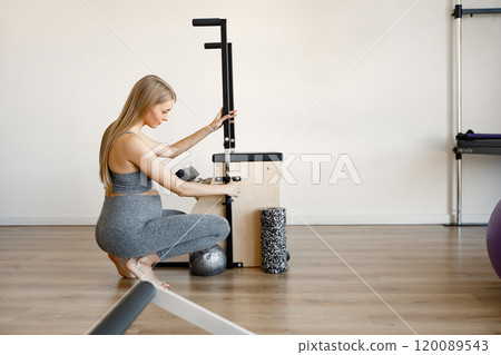 Pregnant woman doing exercises with a special equipment. Fit blonde woman working out in a gym. Woman wearing black sportive leggins and top. 120089543