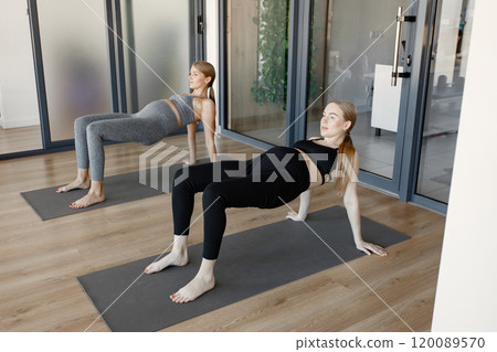 Two pegnant women doing stretching exercise. Fit blonde and brunette women working out in a gym. Women wearing grey and black sportive leggins and tops. 120089570