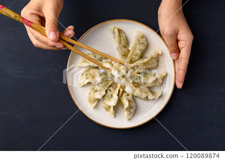 Hand holding chopsticks and eating steamed dumpling filled with pork and vegetables 120089874