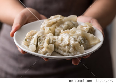 Steamed dumpling filled with pork and vegetables on dish holding by hand 120089879