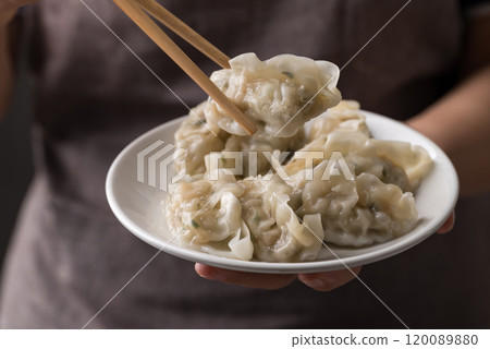 Hand holding chopsticks and eating steamed dumpling filled with pork and vegetables on dish Hand holding chopsticks and eating steamed dumpling filled with pork and vegetables on dish 120089880
