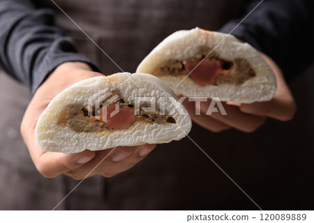 Asian steamed bun stuffed with pork and egg holding by hand and eating 120089889
