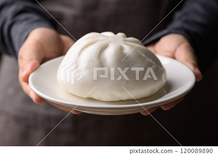 Asian steamed bun stuffed with pork and egg on plate holding by hand 120089890