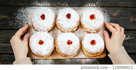 Cooking traditional Hanukkah sufganiyot. Woman sprinkles donuts with powdered sugar. Cooking traditional Hanukkah sufganiyot. Woman sprinkles donuts with powdered sugar. 120090023