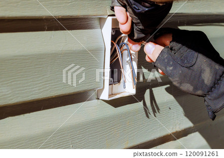 Installing new electrical outlet into wall cavity with gloved hand. Installing new electrical outlet into wall cavity with gloved hand. 120091261