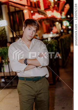A Stylish Young Man is Posing Outdoors Under the Night Sky in a Vibrant City Setting 120092194