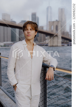 A Stylish Young Man is Posing Confidently Near the Iconic Brooklyn Bridge in New York City 120092232