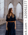 A woman in a stylish dress strikes a captivating pose on the iconic Brooklyn Bridge 120092277