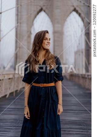 A woman in a stylish dress strikes a captivating pose on the iconic Brooklyn Bridge 120092277