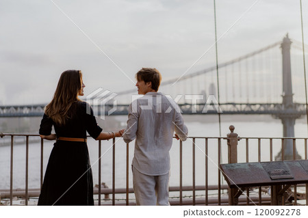 A Loving and Intimate Couple Embraces Tenderly with a Stunning Iconic Bridge in the Background 120092278