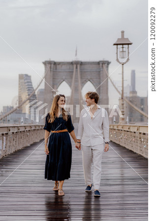 A couple is walking hand in hand across the Brooklyn Bridge as the sun rises beautifully 120092279