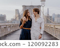 A couple is walking hand in hand across the Brooklyn Bridge as the sun rises beautifully 120092283