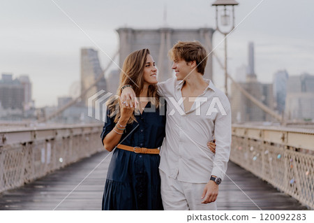 A couple is walking hand in hand across the Brooklyn Bridge as the sun rises beautifully 120092283