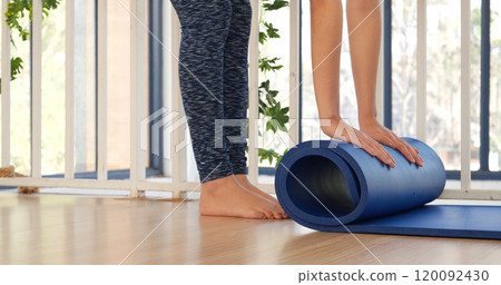 Woman hands rolled up yoga mat on gym floor in yoga fitness training room. Home workout woman close up hands rolling foam yoga gym mat. Woman barefoot home workout sportive healthy lifestyle concept Woman hands rolled up yoga mat on gym floor in yoga fitness training room. Home workout woman close up hands rolling foam yoga gym mat. Woman barefoot home workout sportive healthy lifestyle concept 120092430