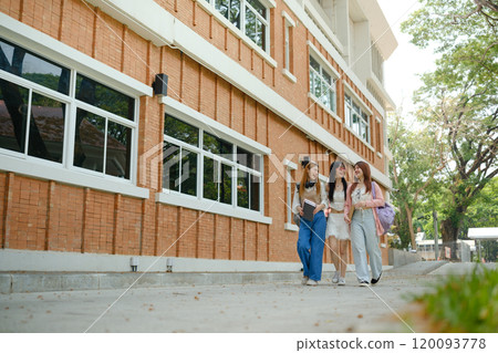 Three young women walking down a sidewalk, one of whom is carrying a backpack Three young women walking down a sidewalk, one of whom is carrying a backpack 120093778