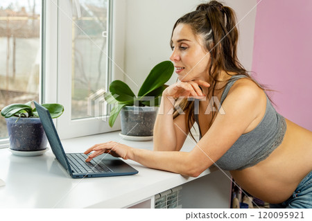 A glowing pregnant woman in casual wear comfortably works from home 120095921