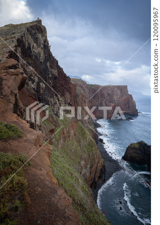 Very steep and tall cliff towering above coast with some rough Atlantic waters, Madeira, Portugal 120095967
