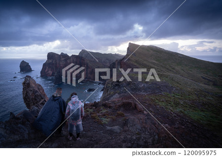 Couple holding hands enjoying view on islandic landscape with high cliffs and storm clouds, Madeira 120095975