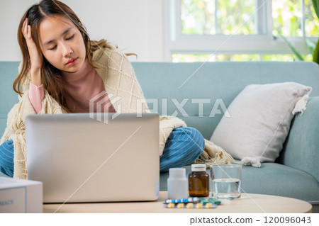 Unwell female working online feeling sick unhealthy, Sick young business woman on sofa suffering from coronavirus covered blanket still work with laptop at home, influenza symptoms, medicine on desk 120096043