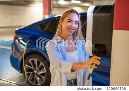 Woman connects her electric car to a charging station in a parking garage Woman connects her electric car to a charging station in a parking garage 120096100