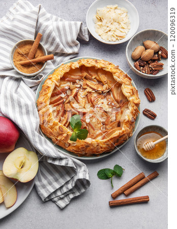 Delicious apple tart with almonds and honey served on a rustic table with fresh apples and spices 120096319