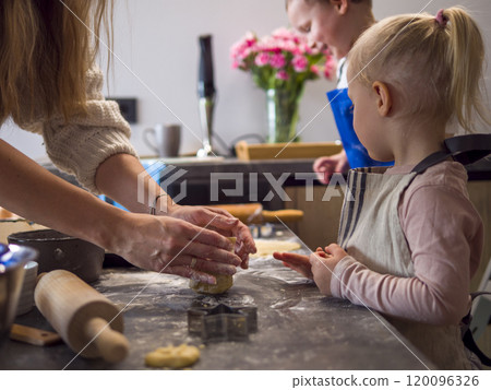 Mother and kids make cookies in lively kitchen, with dough taking shape amidst scattered flour. kids watch eagerly as dough is rolled and cut creating joyful scene centered on dough laughter 120096326