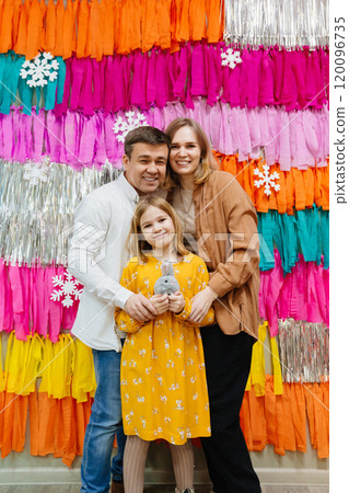 Mom and dad with a teen daughter. a bright multi-colored holiday wall. Mom and dad with a teen daughter. a bright multi-colored holiday wall. 120096735