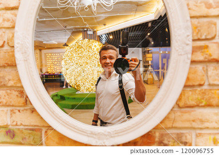 A man with a camera takes his photo in the reflection of a round mirror. 120096755