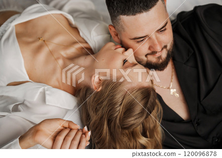 A man and a woman in silk pajamas are lying on a bed. 120096878