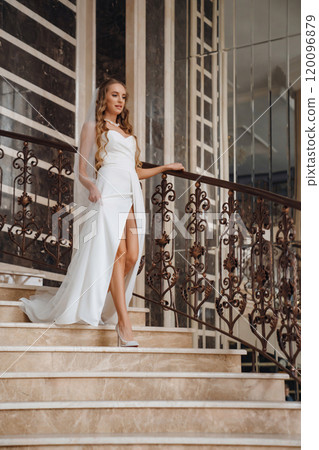 Beautiful blonde bride in a simple elegant wedding dress going down the stairs. Beautiful blonde bride in a simple elegant wedding dress going down the stairs. 120096879