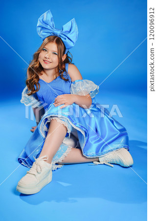 Cute teenage girl in blue doll dress with big blue bow posing lying on the floor Cute teenage girl in blue doll dress with big blue bow posing lying on the floor 120096912