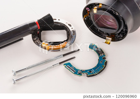 A broken lens of a professional camera and repair tools on a white table. A broken lens of a professional camera and repair tools on a white table. 120096960