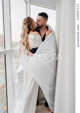 A gentle and romantic man and woman wrapped in a blanket on the windowsill 120097115