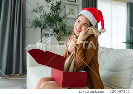 Young Asian woman wearing Christmas hat and opening a gift box Young Asian woman wearing Christmas hat and opening a gift box 120097201