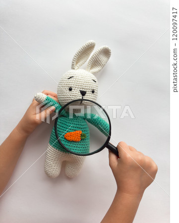 Child examining crochet bunny with magnifying glass 120097417