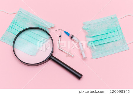Broken Medical Syringe and Green Torn Medical Face Mask with Magnifying Glass 120098545