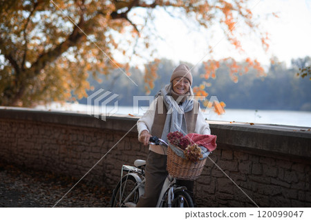 Seniow woman riding bicycle in autumn park, enjoying peaceful moment outdoor alone. 120099047