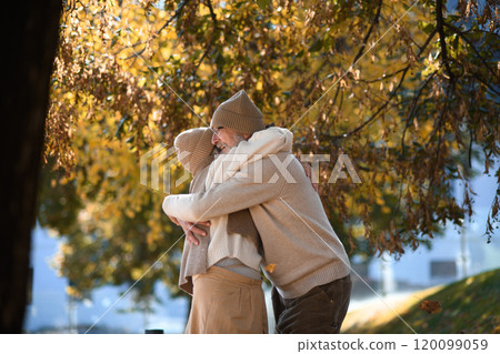 Portrait of beautiful senior couple during walk in autumn park. Elderly husband and wife are embracing each other. Portrait of beautiful senior couple during walk in autumn park. Elderly husband and wife are embracing each other. 120099059