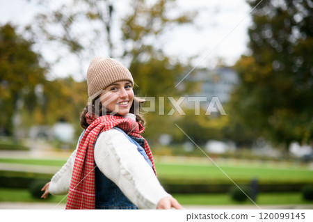 Portrait of a beautiful woman in the middle of autumn park, standing with outstretched arms, enjoying seasonal weather around her. 120099145