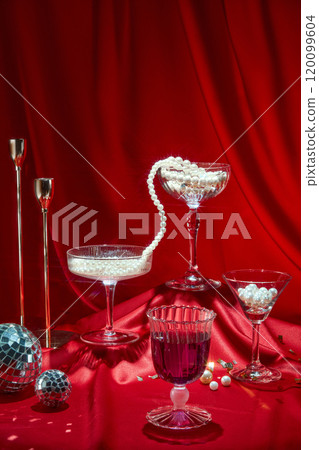 A front view of an upper crimson surface placed glasses, disco balls, pearl threads, and confetti dispersed across it against a red background. A picture template for a party theme. 120099604