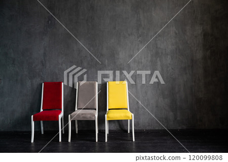 Three multicolored chairs in the interior of an empty gray room 120099808
