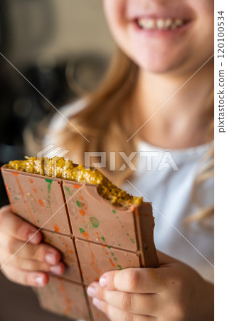 Dubai chocolate with pistachio paste and kataifi dough in hands of little girl. Confectionery handmade sweets at home in the kitchen. Dubai chocolate with pistachio paste and kataifi dough in hands of little girl. Confectionery handmade sweets at home in the kitchen. 120100534