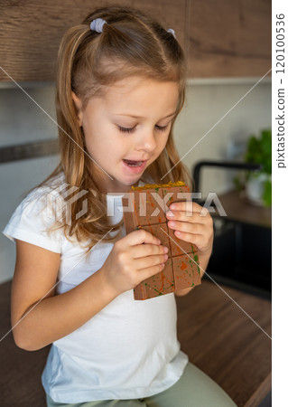 Little girl eating Dubai chocolate with pistachio paste and kataifi dough. Confectionery handmade sweets at home in the kitchen. Little girl eating Dubai chocolate with pistachio paste and kataifi dough. Confectionery handmade sweets at home in the kitchen. 120100536