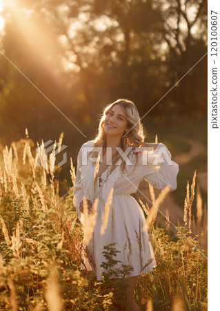 A woman is standing in a field of tall grass, wearing a white dress A woman is standing in a field of tall grass, wearing a white dress 120100607