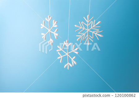 Snowflake made from cotton swabs hanging on string against blue background. Minimalist winter decoration. Christmas and winter holidays concept for greeting card, poster, and seasonal design 120100862
