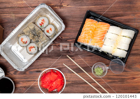 ordered food from an Asian cafe, fried rolls and tuna rolls, with ginger, soy sauce and wasabi in plastic packaging, on a wooden background 120101443