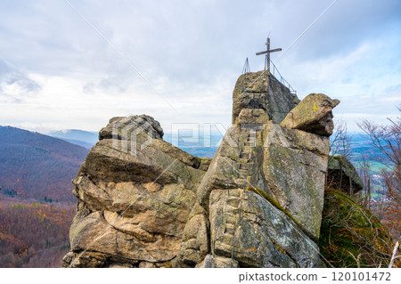 The rocky Oresnik formation features a lookout point and wooden summit cross, offering panoramic views of the Jizera Mountains in Czechia on a cloudy day. 120101472
