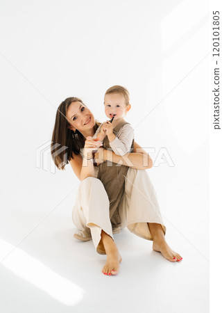 Young woman is holding a baby in her arms. Son is smiling and mother is smiling back. Warm and loving 120101805